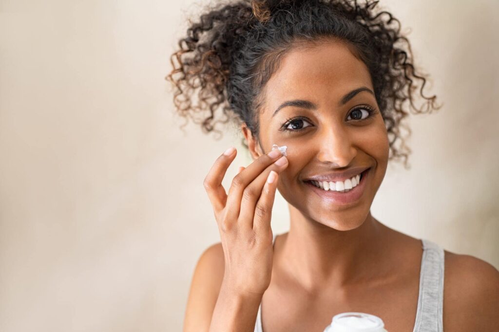 Woman smiling while applying skin care to her cheek