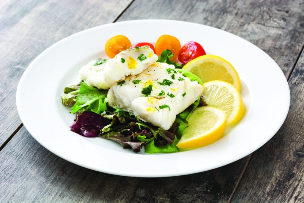 A piece of cod on a bed of lettuce and lemon slices.