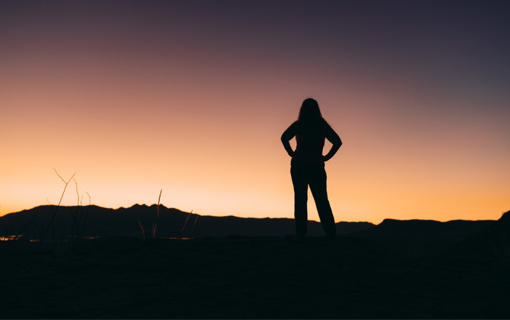 Woman Stands On Top of a Mountain with Sunset in the Background